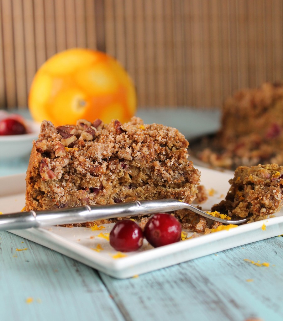 a side view of a triangle slice of coffee cake with a crumb topping and fresh cranberries