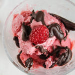 birdseye view of a clear glass filled with deep pink ice cream slathered in a fudge chocolate sauce