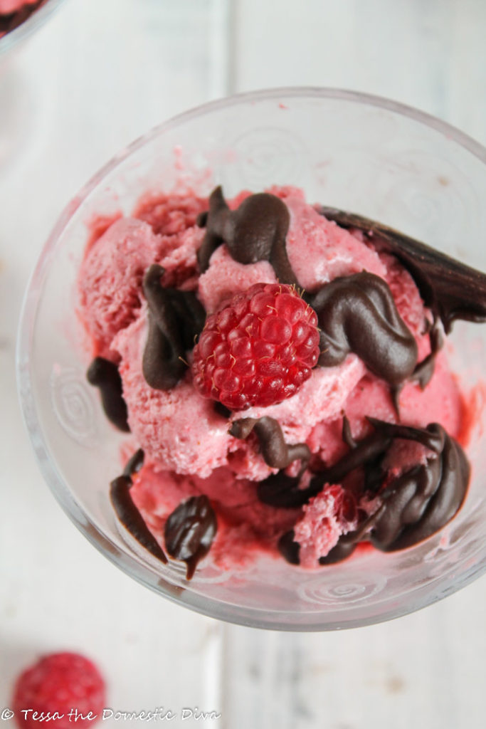 birdseye view of a clear glass filled with deep pink ice cream slathered in a fudge chocolate sauce
