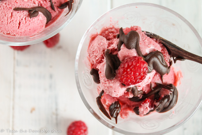 birds eye view of two fluted clear glass cups filled with strawberry ice cream drizzled with a chocolate sauce and an dark wooden spoon