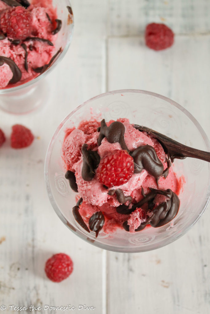 two glass tapered bowls filled with dairy free strawberry ice cream and drizzled with a fudgey chocolate sauce