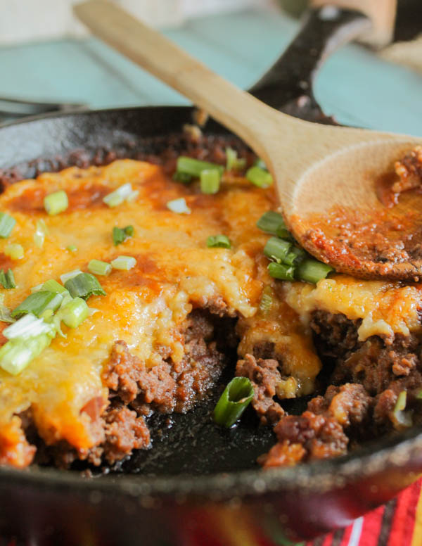 spooned up serving on tender ground beef with a chewy tamale topping and a garnish of green onions and a wooden spoon