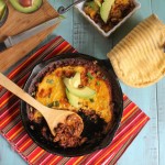 birdeye view of a cast iron skillet filled with savory ground beef, pinto beans and topped with a tamale masa and cheese