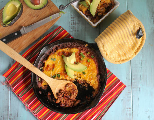 birdeye view of a cast iron skillet filled with savory ground beef, pinto beans and topped with a tamale masa and cheese