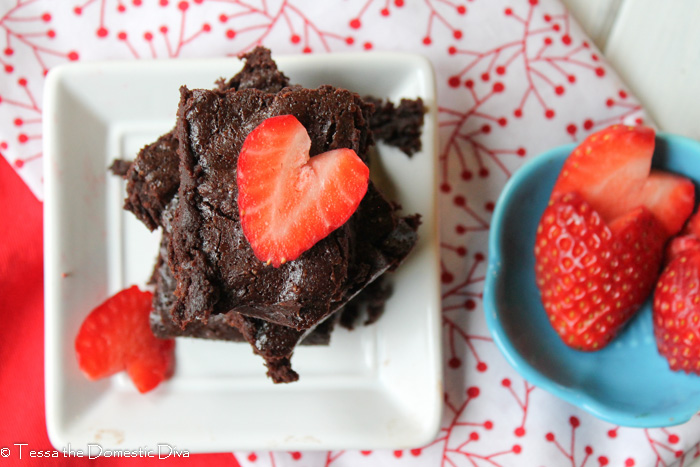 overhead view of a square white plate with a square of chocolate brownie topped with a fresh heart shaped strawberry
