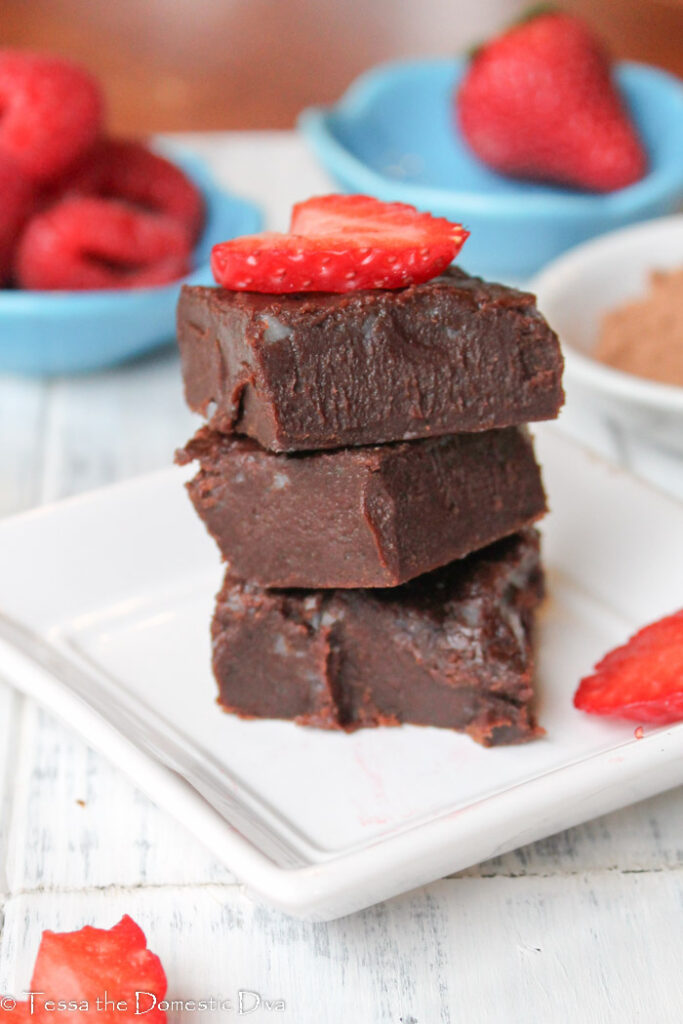 a stack of three egg free gluten free chocolate brownies on a white plate with fresh sliced strawberries