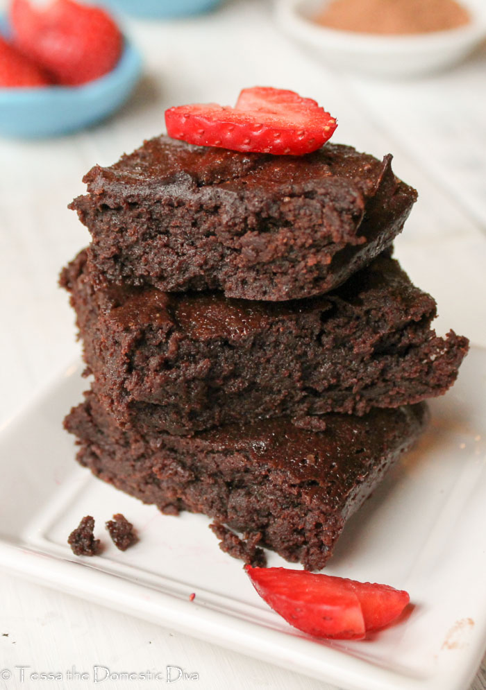 three stacked cocoa powder brownies on a white plate with a heart cut fresh strawberry slice