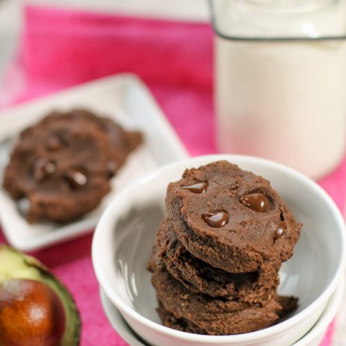 dense and fudgy stack of chocolate cookies studded with molten chocolate chips and halved avocado half on the left