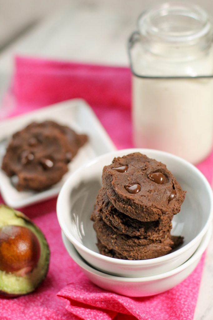 dense and fudgy stack of chocolate cookies studded with molten chocolate chips and halved avocado half on the left