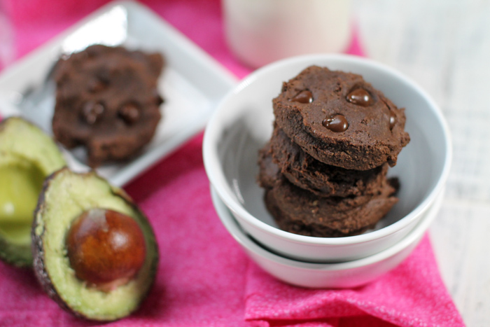 two stacked white bowls with a stack of chocolate chocolate cookies and a fresh halved avocado on the side
