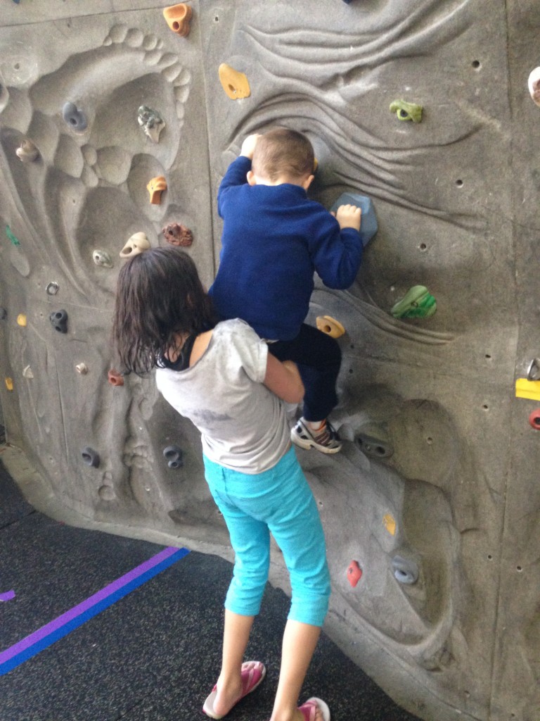 older sister helping younger brother to climb a rock wall