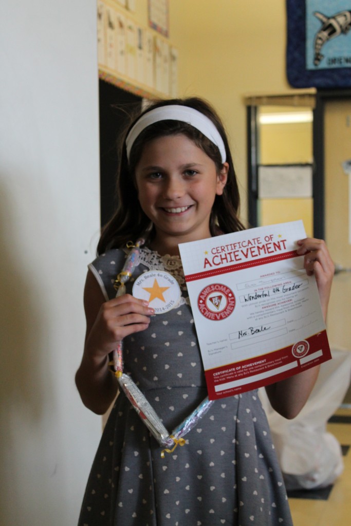 10 year old girl holding a certificate of achievement in a school hallway