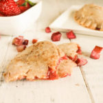 overhead shot of strawberry rhubarb hand pies arranged on a white washed board with diced fresh rhubarb and fresh whole strawberries