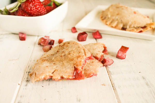 overhead shot of strawberry rhubarb hand pies arranged on a white washed board with diced fresh rhubarb and fresh whole strawberries