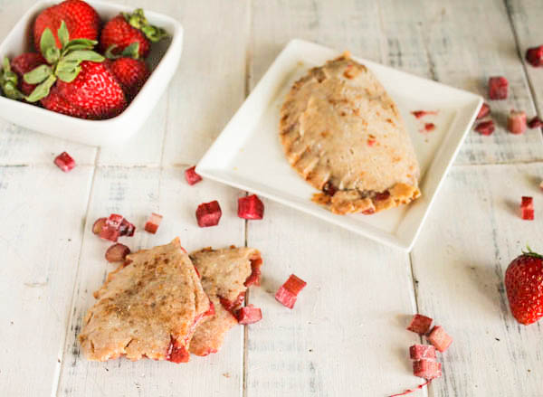 overhead shot of strawberry rhubarb hand pies arranged on a white washed board with diced fresh rhubarb and fresh whole strawberries