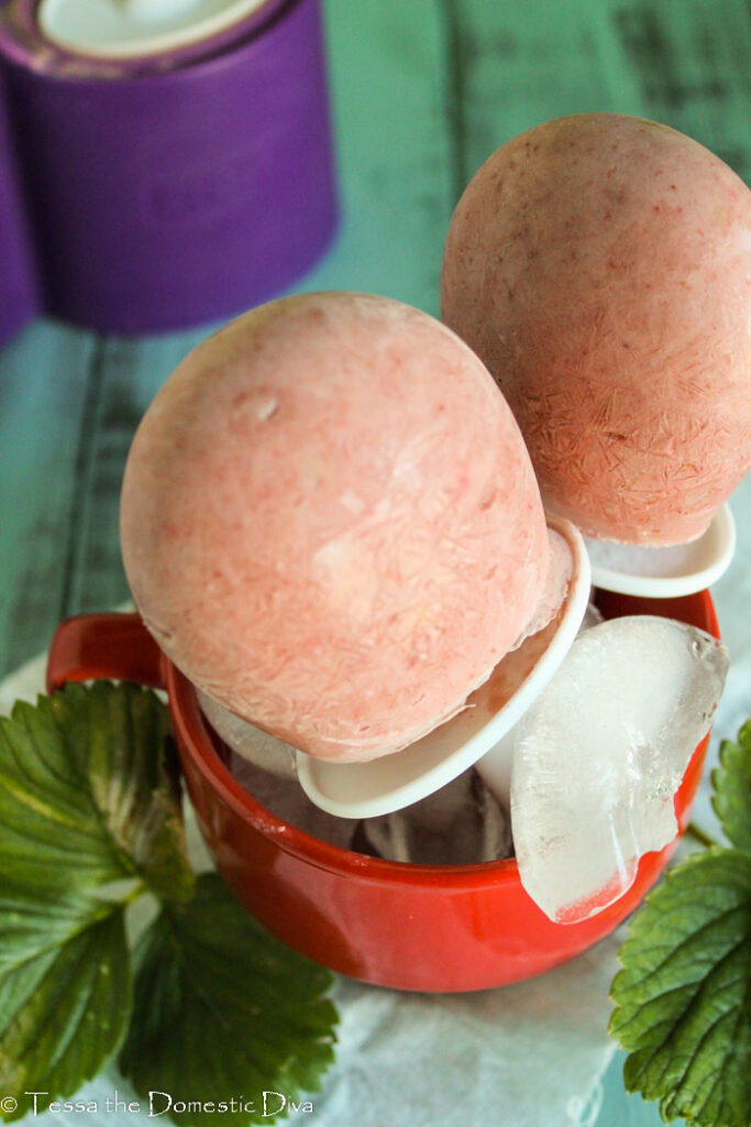 2 strawberry popsicles in a red mug.