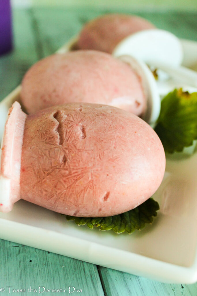 three strawberry popsicles laying their sides on a white plate.