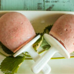 three strawberry cream popsicles from overhead arranged on a white plate with strawberry leaf garnish