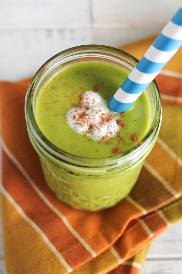 a mason jar filled with a creamy green smoothie with a dollop of coconut cream and sprinkle of cinnamon
