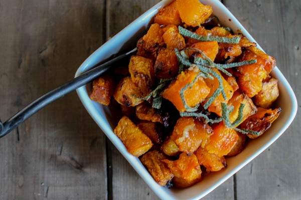 overhead shot of whole30 roasted butternut squash in a white square bowl on a dark wooden surface