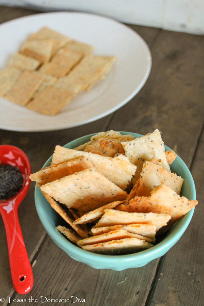 a birds eye view of a small blue bowl filled with homemade cheese crackers with a red ceramic measuring spoon