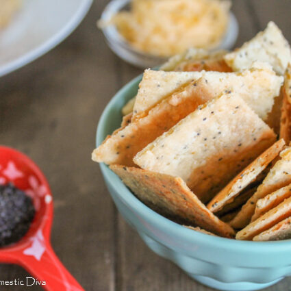 a bowl full of cheese cracker made from scratch with a red measuring spoon on a dark wooden board