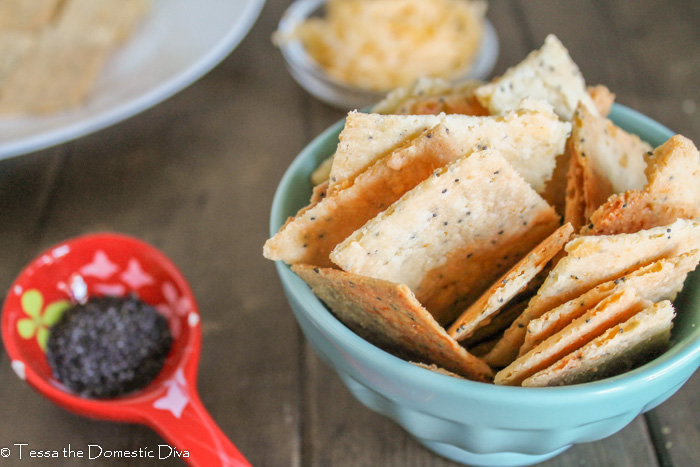 a bowl full of cheese cracker made from scratch with a red measuring spoon on a dark wooden board