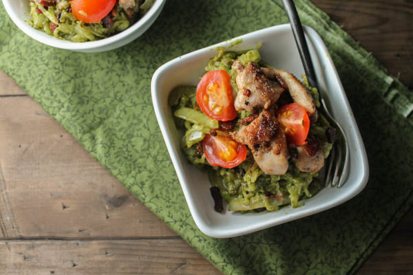 overhead shot of two white bowls filled with green pesto spaghetti squash noodles topped with crispy bacon, chicken thighs, and sliced cherry tomatoes