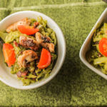 overhead shot of two white bowls filled with green pesto spaghetti squash noodles topped with crispy bacon, chicken thighs, and sliced cherry tomatoes