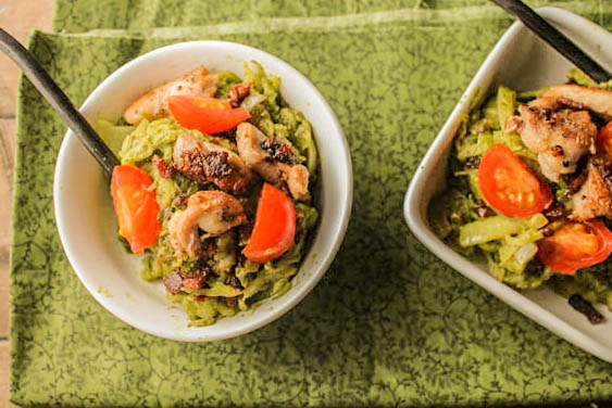 overhead shot of two white bowls filled with green pesto spaghetti squash noodles topped with crispy bacon, chicken thighs, and sliced cherry tomatoes