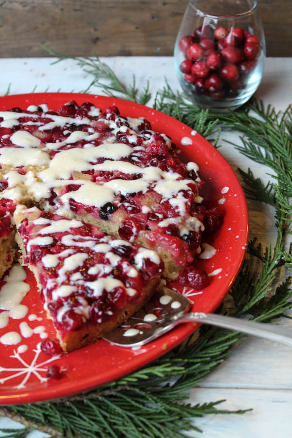 cranberry topped upside down cake atop evergeen boughs and drizzled with a white glaze