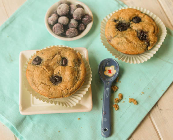 overhead shot of blueberry muffins on a turquoise linen baked in mint green paper liners with a bowl of fresh blueberries