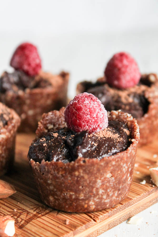 a grouping of mini no bake chocoalte tarts in a nut crust with a fresh raspberry topping and a white background