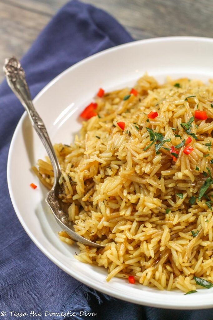 golden rice pilaf garnished with fresh parsley and minced red pepper in a white bowl with a navy linen