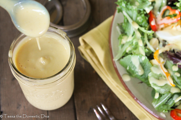creamy yellow hney mustard dressing drizzling from a ceramic spoon into a half pint mason jar