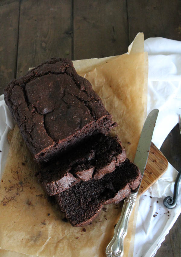 sliced chocolate zucchini bread from overhead on a piece of parchment and a white cloth with a silver knife and two forks