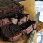 close up of sliced chocolate zucchini bread on a brown parchment and a silver knife