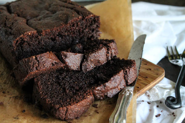 close up of sliced chocolate zucchini bread on a brown parchment and a silver knife