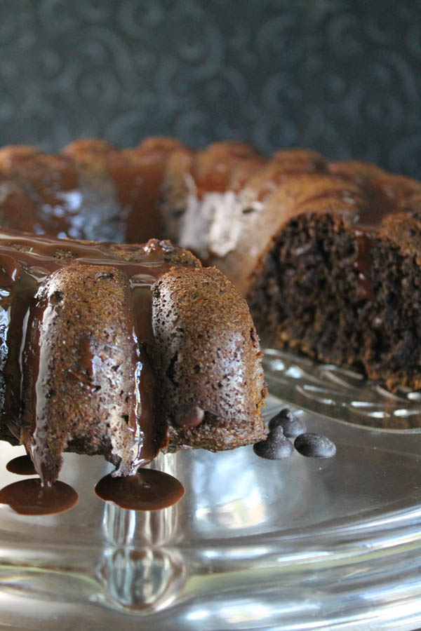 a dark chocolate bundt cake on a glass cake plate with melted chocolate drizzle