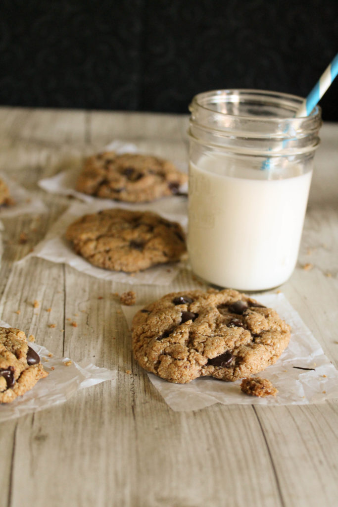 multiple chocolate chip cookies atop parchment paper squares with a mason jar of milk nearby