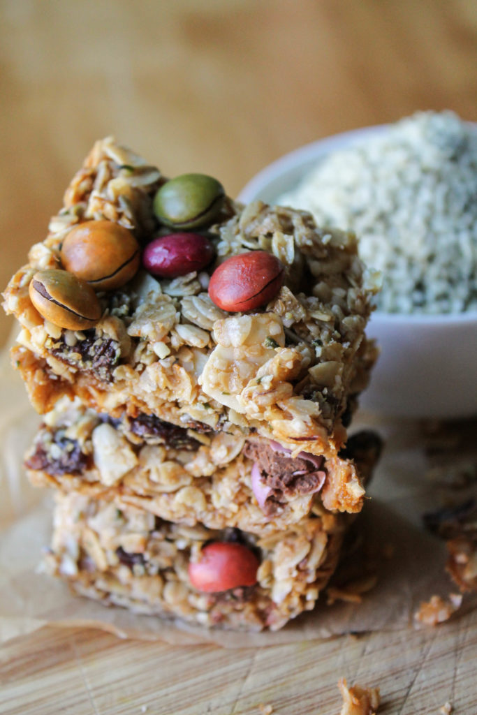 three square homemade healthy granola bars stacked on a bamboo cutting board.