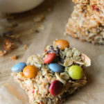 a hemp granola bar with dye free m & m's on parchment and a wooden cutting board.