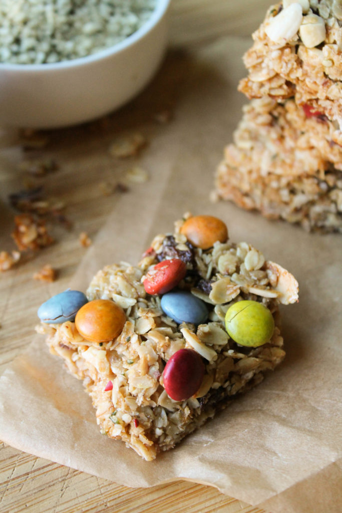 a hemp granola bar with dye free m & m's on parchment and a wooden cutting board.