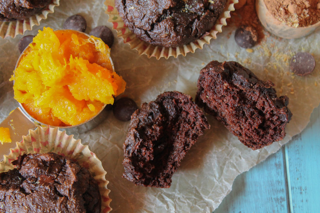overhead close up of a rich chocolate brown butternut squash muffin torn in half next to a scoop of cooked squash puree