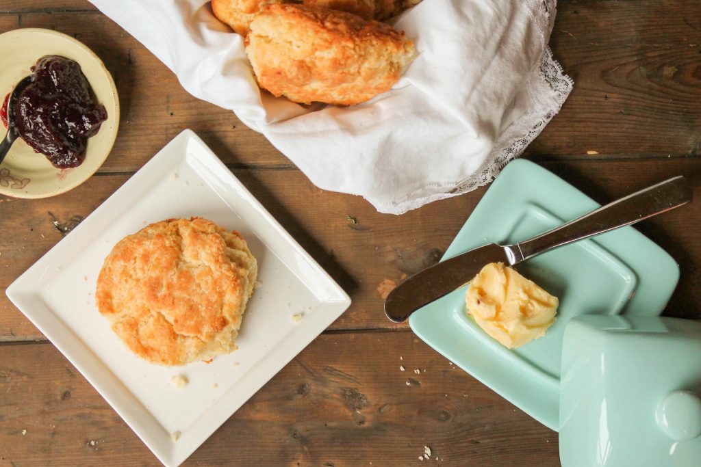 a fluffy biscuit on a white plate from overhead on a dark wooden surface with a turquoise butter dish.