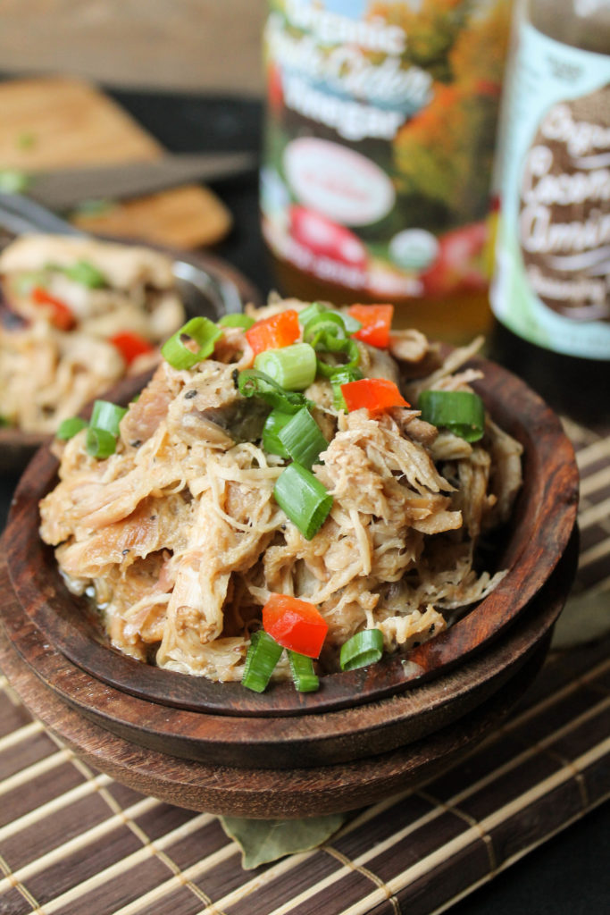 tender shredded adobo chicken garnished with green onion and diced red bell pepper in a dark wooden bowl