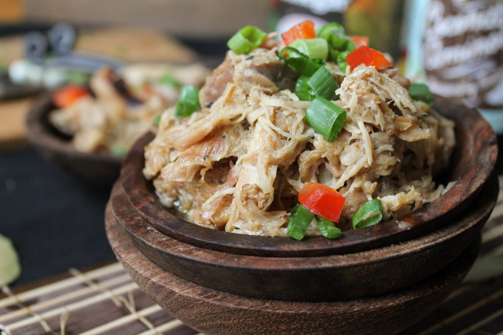 horizontal image of shredded Filipino chicken in three stacked dark wooden bowls with a sliced green onions and diced red bell pepper