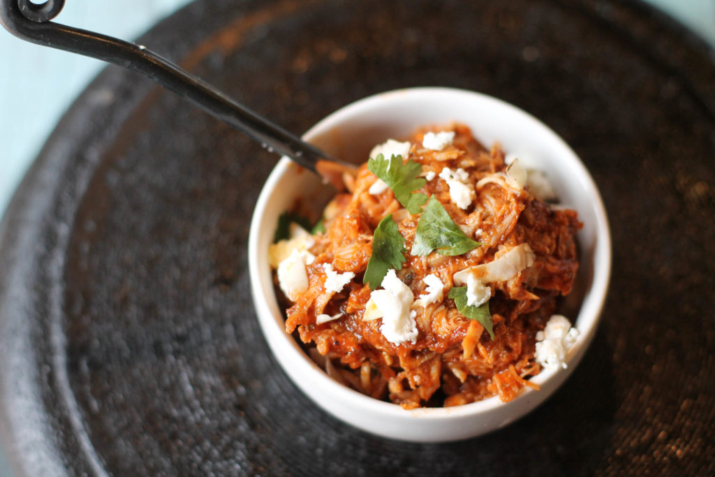 instant pot shredded chicken tings in a small white bowl topped with cilantro and cotija cheese from above