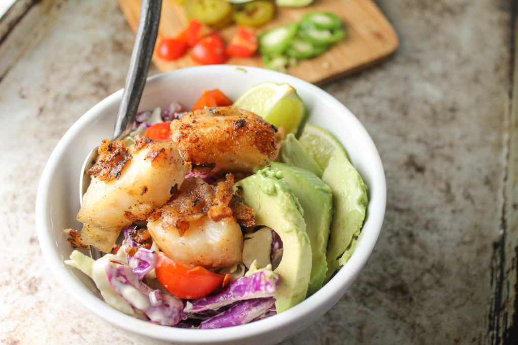 white bowl on rustic cookie sheet filled with cabbage slaw and pan fried pieces of fish and avocado