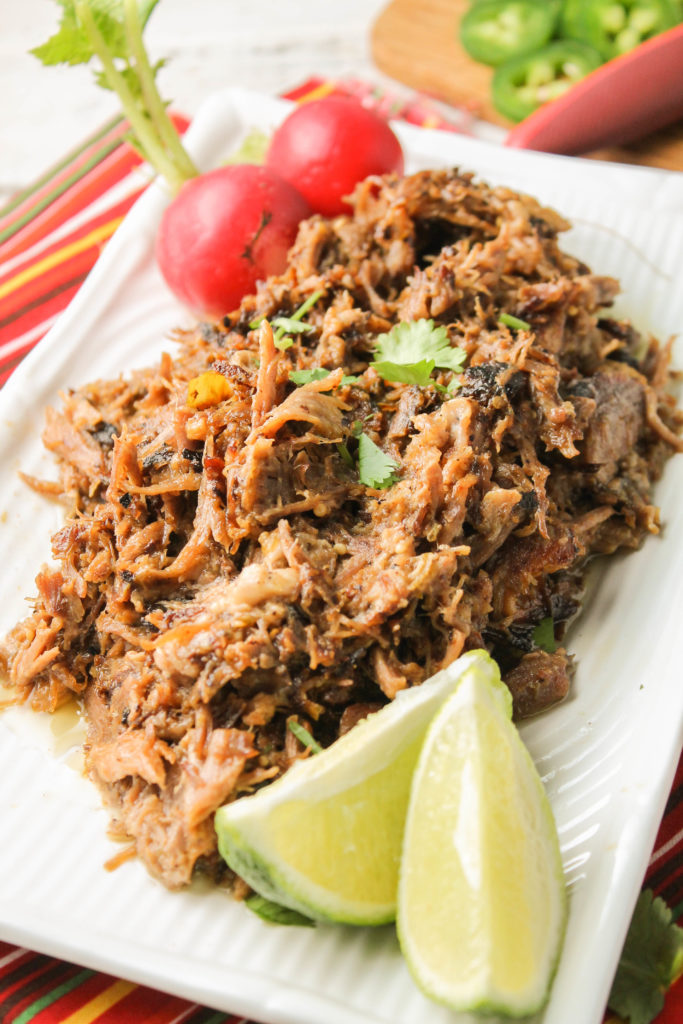 crispy carnitas atop a white plate with fresh lime wedges and whole red radishes